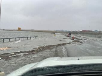 A photo taken from the driver's seat of a white truck showing a road partially flooded and littered with debris