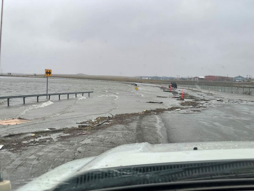 A photo taken from the driver's seat of a white truck showing a road partially flooded and littered with debris