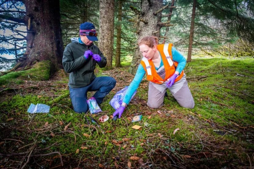 Two people kneeling in the woods, studying something on the ground