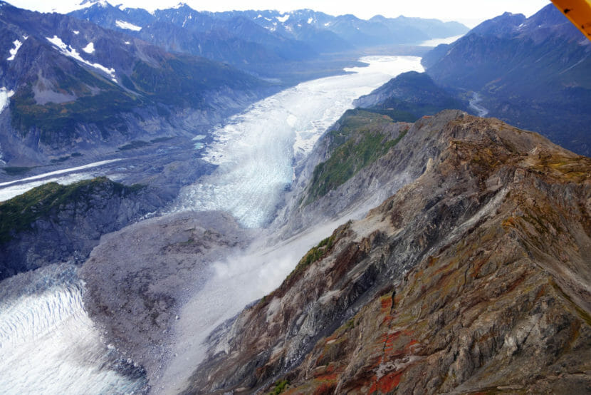 A fresh landslide, with dust still in the air, piled up on a glacier below a steep fjord wall