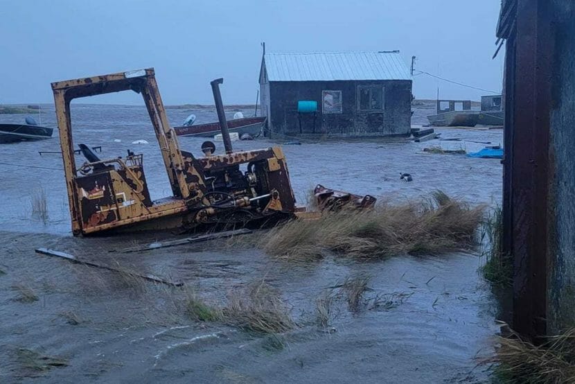 A bulldozer sitting in a few feet of water with a flooded house in the background