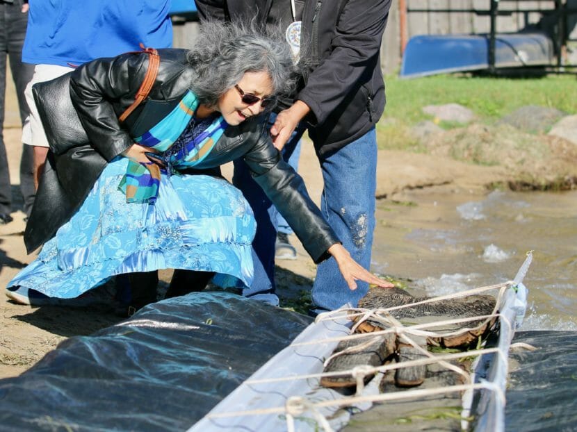 A smiling woman bends down to touch the ancient canoe