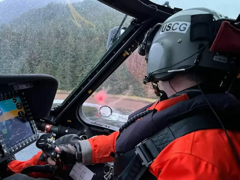 A shot taken over a pilot's shoulder shows a beach with a bright red marker on it.