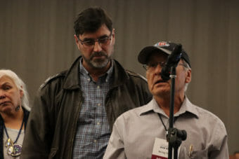 A man speaks into a microphone while others wait in line behind him.