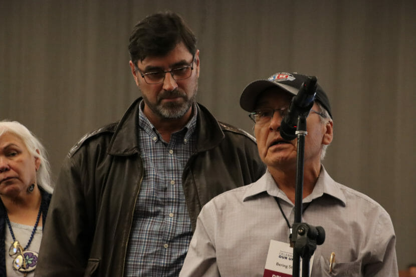 A man speaks into a microphone while others wait in line behind him.