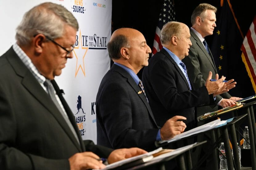 Seen from the side, four candidates for Alaska governor stand behind lecterns on a stage
