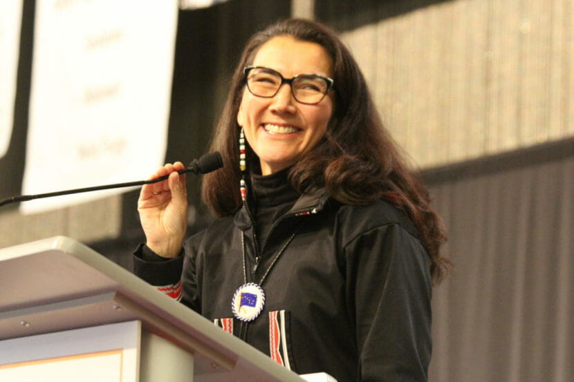 Mary Peltola stands smiling and holding a microphone behind a lectern