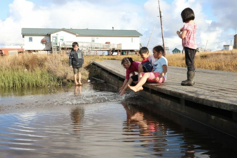 Five children standing on and around a dock in a pond
