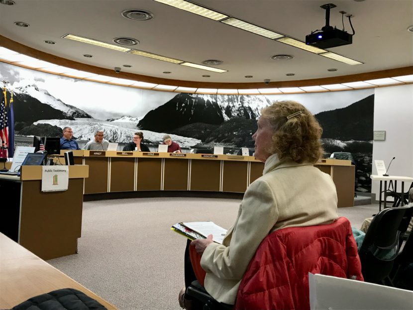 A woman sits in a folding chair facing commission members