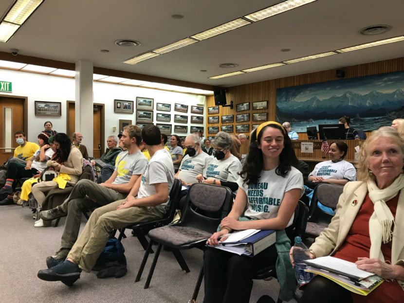 People sitting in rows of folding chairs in a city meeting hall.