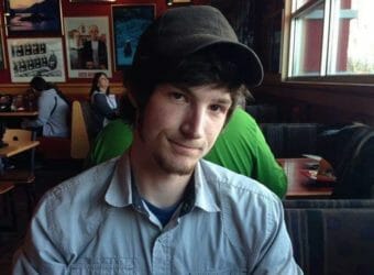 A young man in a baseball cap sitting in a restaurant booth, smiling