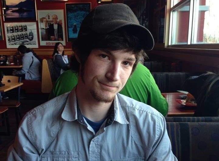 A young man in a baseball cap sitting in a restaurant booth, smiling