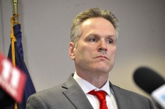 Gov. Dunleavy stands with an Alaska flag in the background