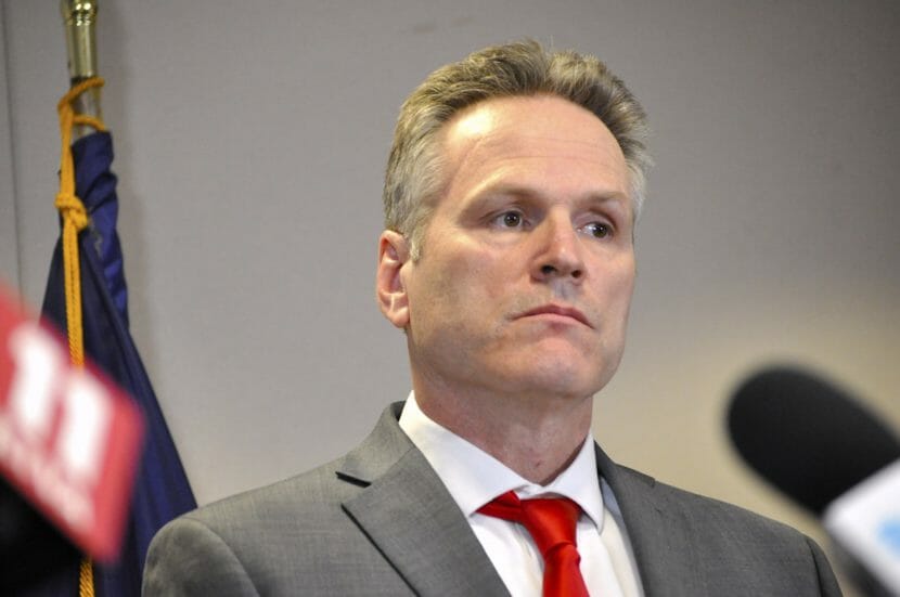 Gov. Dunleavy stands with an Alaska flag in the background