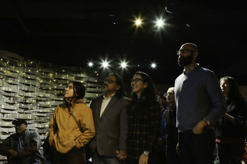 Mary Peltola and three others stand in a row, looking up at a monitor that's offscreen.