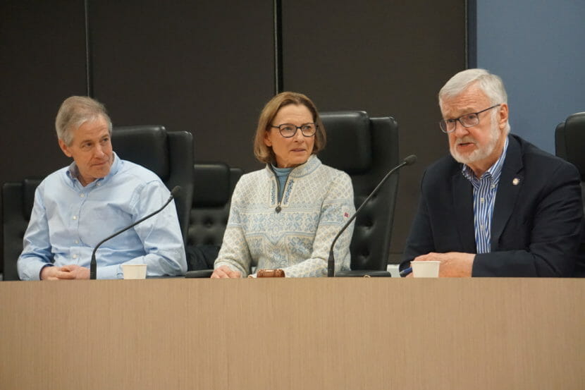 A woman and two men sit behind a long desk.