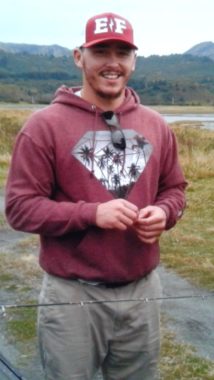 A man in a red sweatshirt stands smiling with a fishing rod
