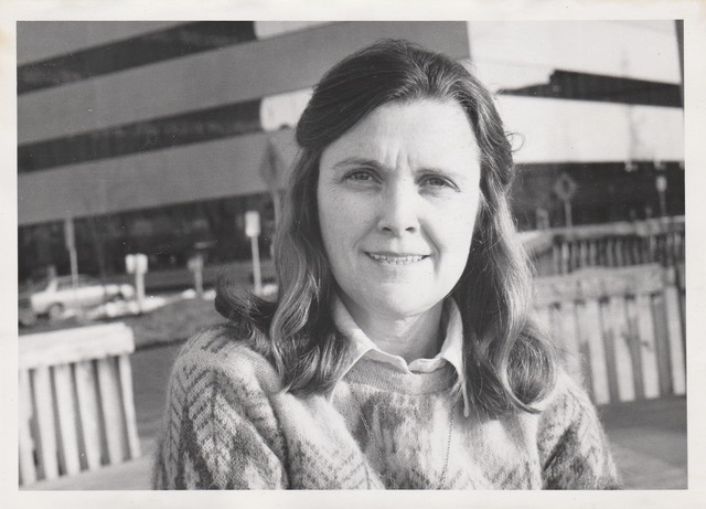 A black-and-white photo of a woman in front of a large, concrete building