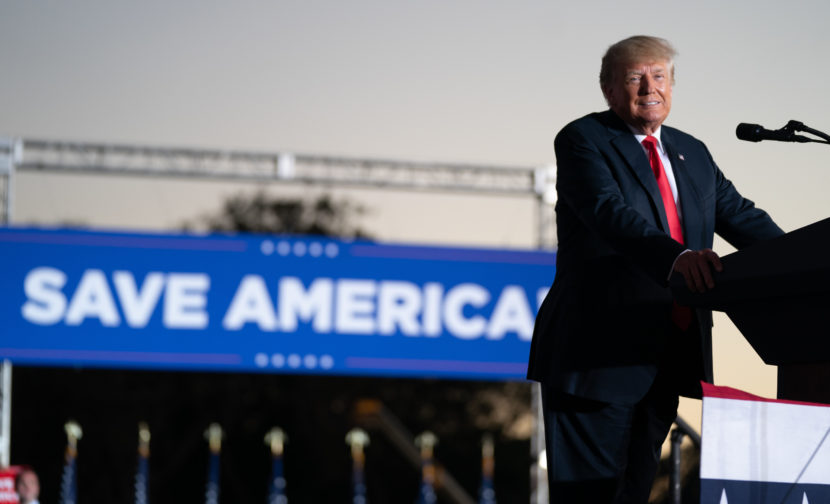 Donald Trump speaks in front of a banner that says "save America"