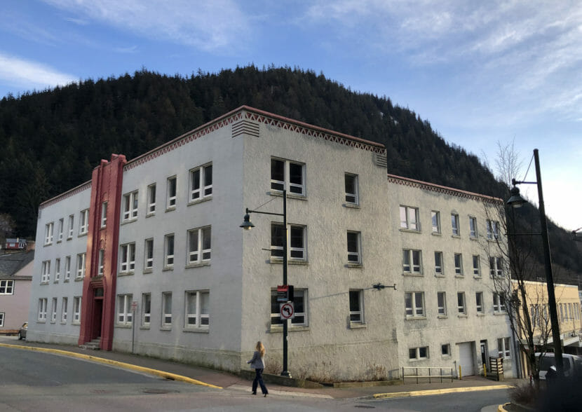 A woman walking past a blocky, grey-and-red office building.