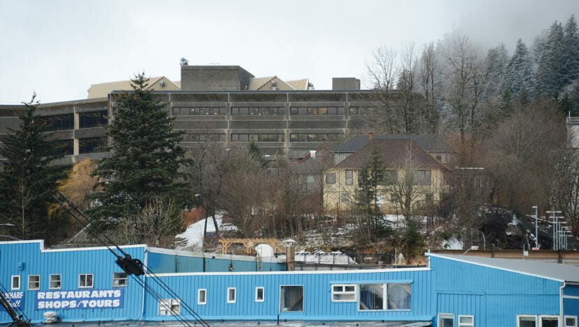 Older houses sit on a small hill with a large government building behind it.