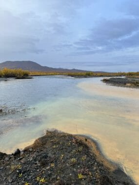 Orange water meets clear water at the confluence of two Arctic streams.