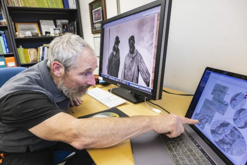 A man points at a map and photos on a laptop.