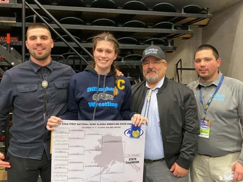 A high school girl stands with three male coaches. 