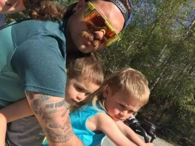 A man with a mullet hugs two young boys with mullets.