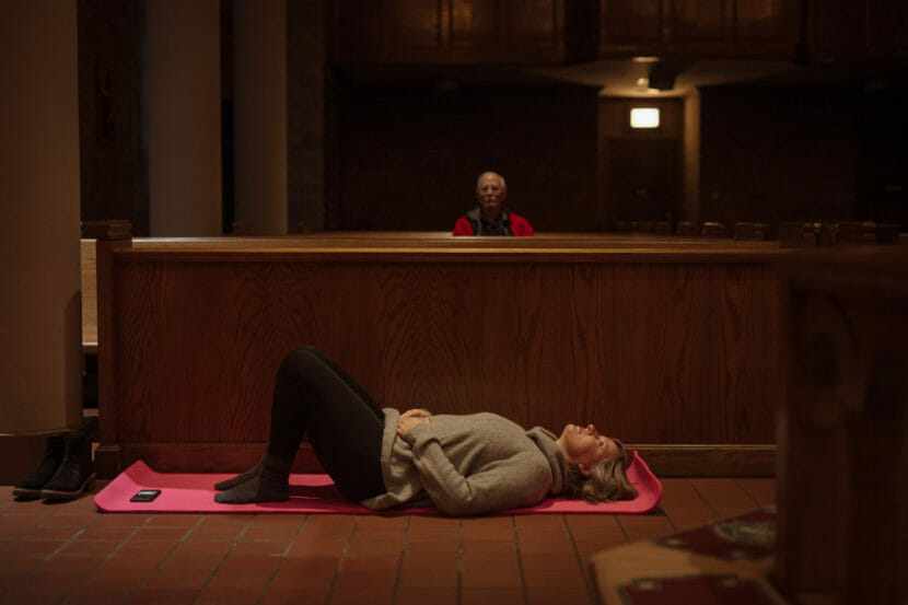 A woman lies on a yoga mat among church pews