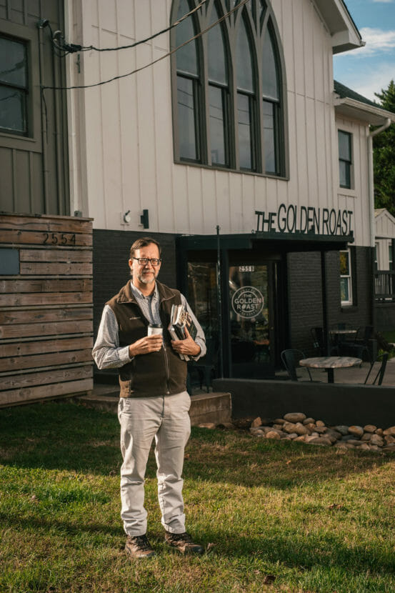 A man in a fleece vest stands outside a coffee shop.