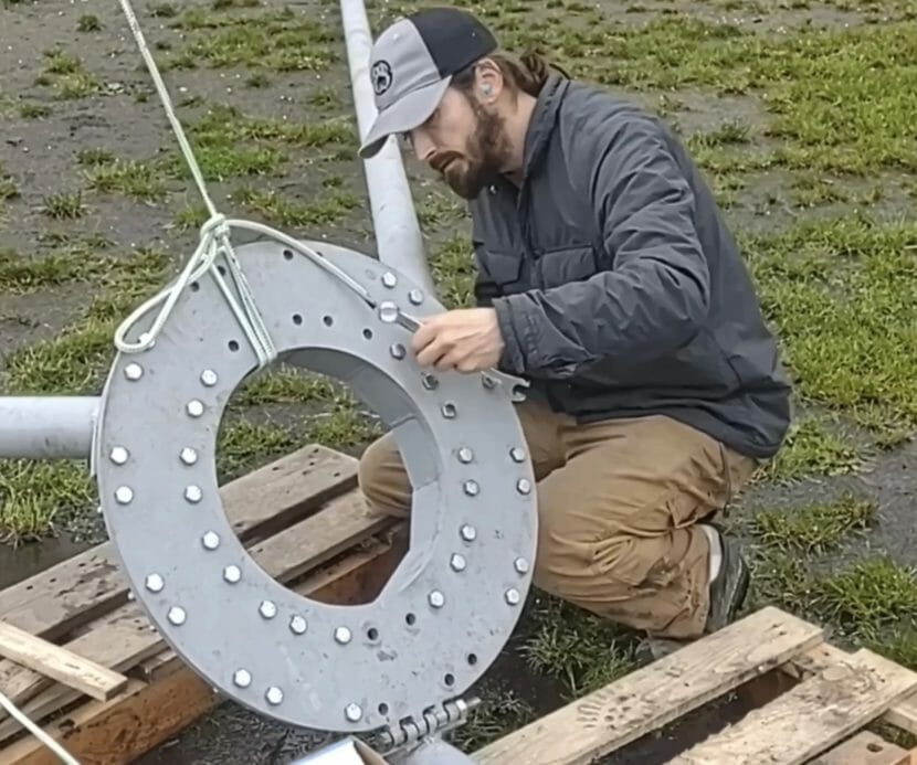 A man in a baseball cap studies a large donut-shaped piece of metal