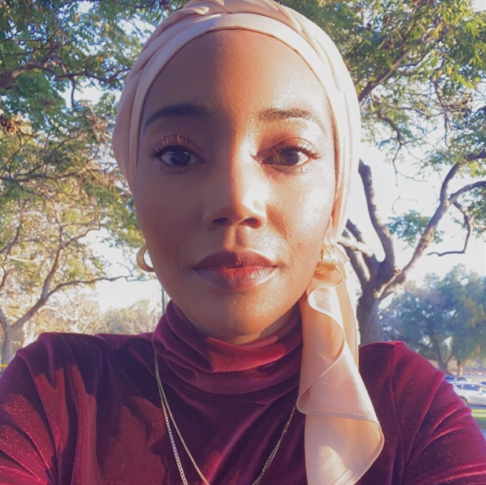 A photo of Ajia Munns in a red shirt wearing a cross with trees behind