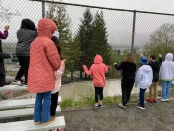 Children in raincoats look through a tall fence.