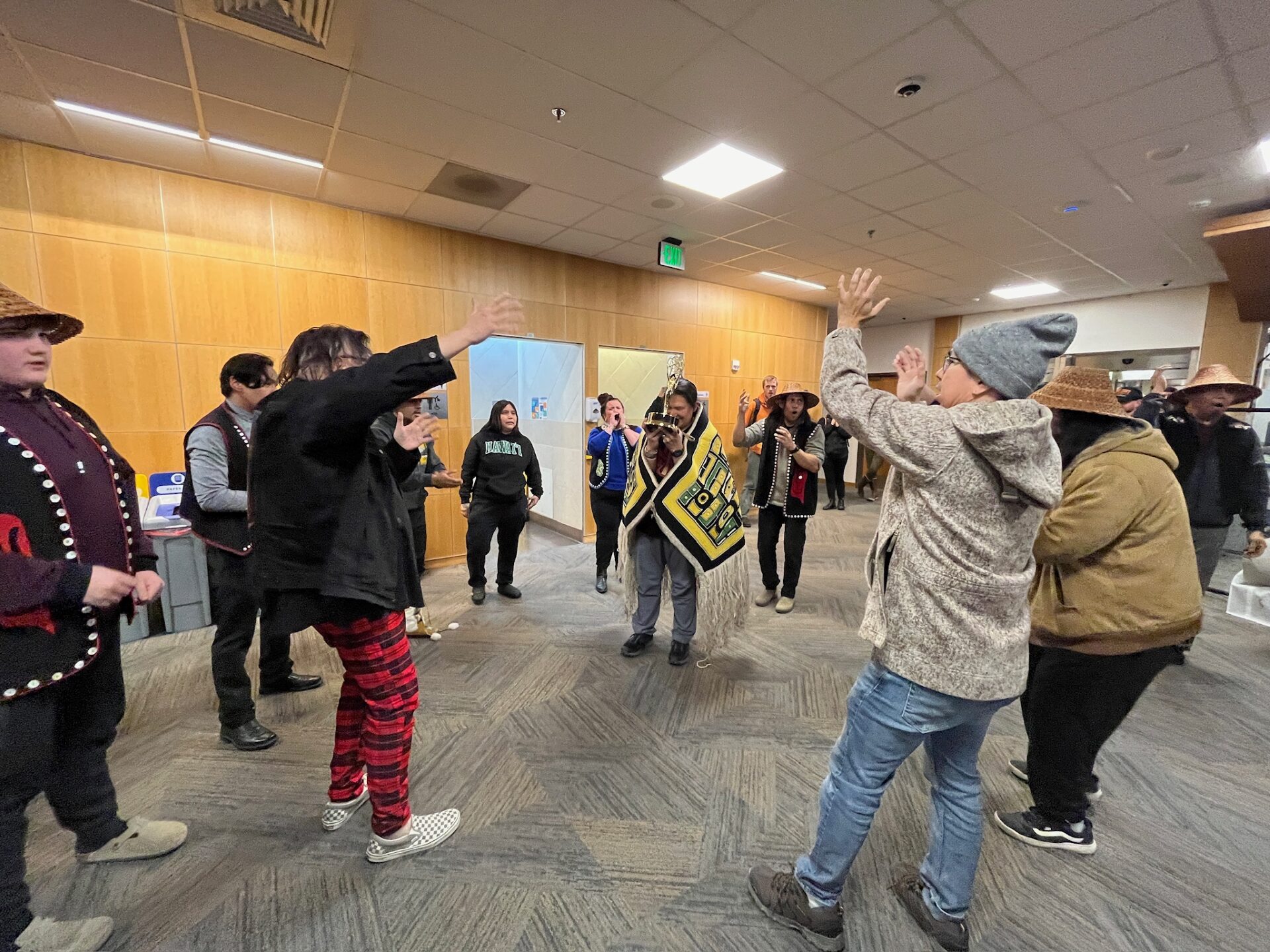 X'unei Lance Twitchell holding his Emmy Award and circled by community members welcoming him at the Juneau Airport. 
