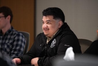 A man in a black coat speaks at a conference.