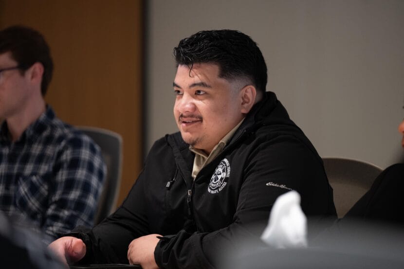 A man in a black coat speaks at a conference. 