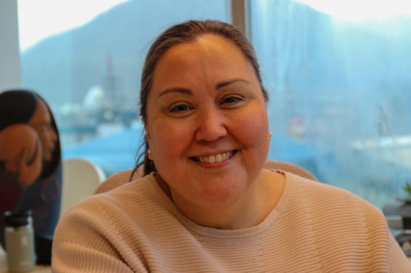 A woman dressed in an off-white sweater and pearl earrings smiles for a photo.