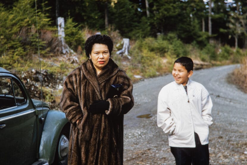 A woman in a fur coat looks at the photographer, while a boy smiles at her. From the Cyril George Photo Collection.