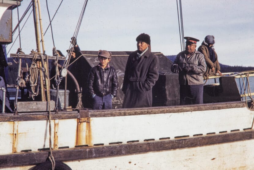 Two men and a boy look on from a boat. From the Cyril George Photo Collection.