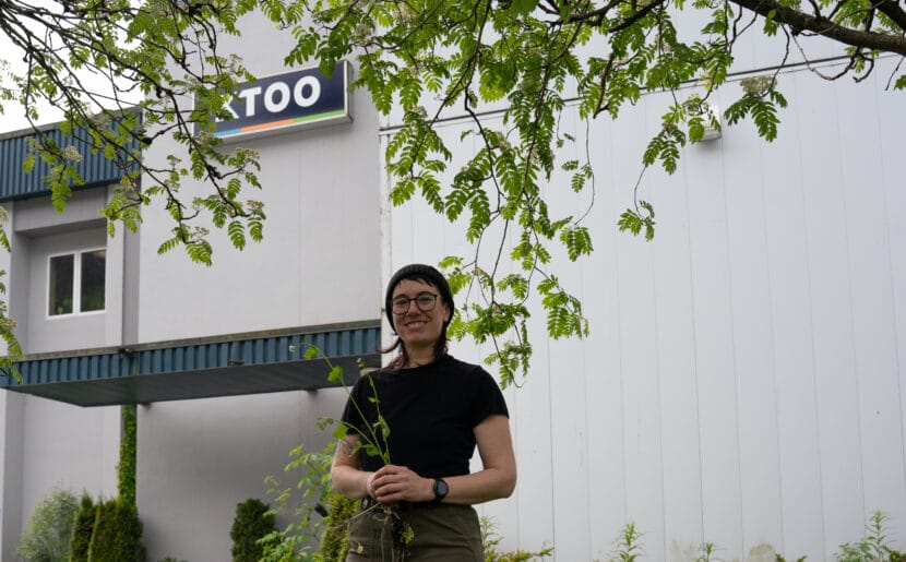 Emily Reed clutches invasive garlic mustard beneath an invasive European mountain ash tree in front of KTOO. (Photo by Alix Soliman/KTOO)
