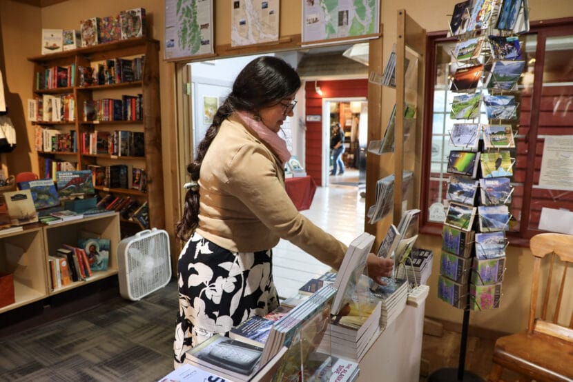 A woman with a long braid and glasses looks at covers of books in a bookstore.