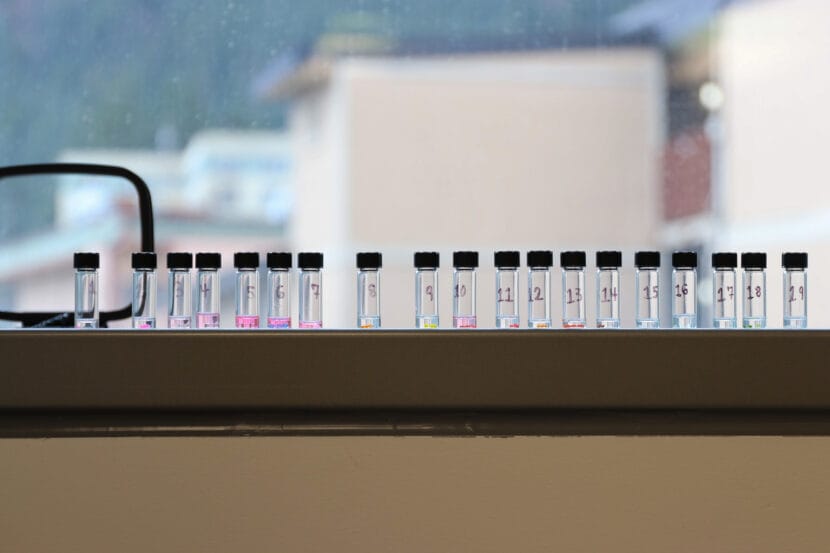 Beads of various colors are placed in numbered glass vials filled with clear liquids on the windowsill of the Alaska State Museum objects conservation lab.