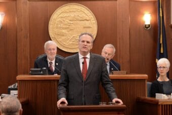 A man stands at a podium with the Alaska state seal behind him