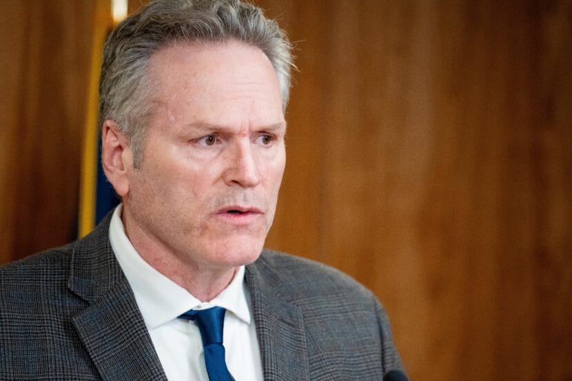 Man in grey suit standing behind microphones