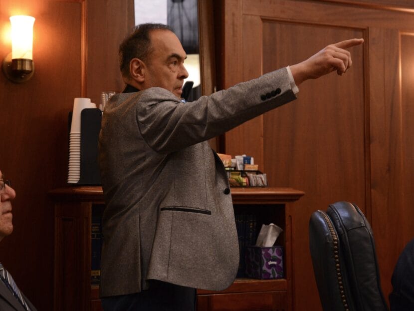 A man in a gray suit seen in profile points upward