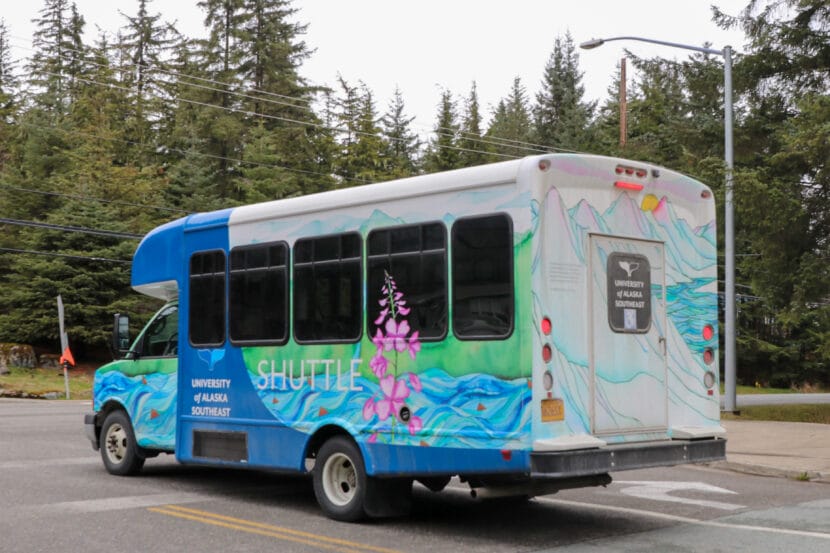 A blue and white bus with fireweed painted on the side that says "University of Alaska Southeast" with a whale tail logo.