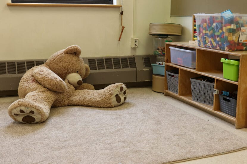 A large teddy bear rests on the ground next to a shelf full of toys at Floyd Dryden Middle School.