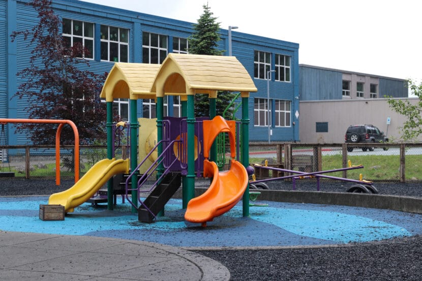 A green metal play structure with two slides on a blue rubber flooring.