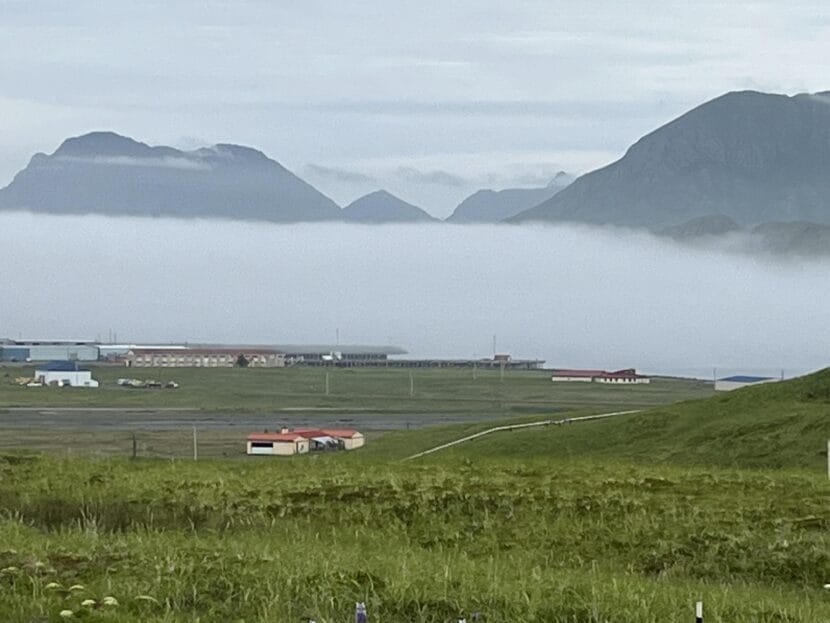 looking down on buildings in the distance from a green hillside. mountains and fog in the background